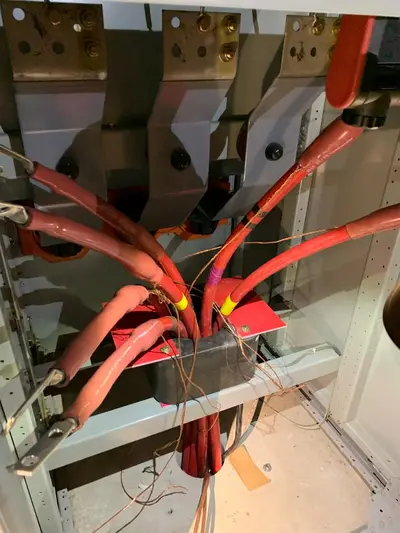 Three shielded medium-voltage cable terminations inside a switchgear cubicle: heat-shrink stress cones, compression lugs bolted to the bus pads, shield drain wires collected down to the enclosure ground bar.