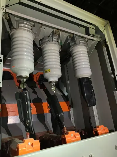 Three porcelain bushings on a medium-voltage switch, phase conductors landed and taped under boots, insulated bus supports behind.