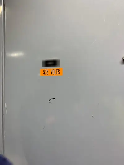 A motor control center door carrying a 575 VOLTS marking below its designation plate, which is masked.