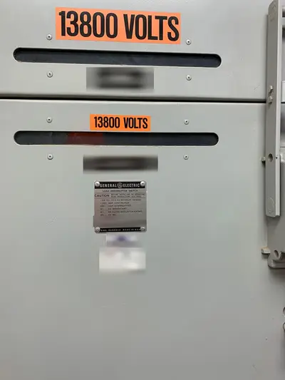 A second cubicle in the same switchgear lineup, 13800 VOLTS marked on both door panels with the load-interrupter rating plate at center. Designation, asset and service plates are masked.