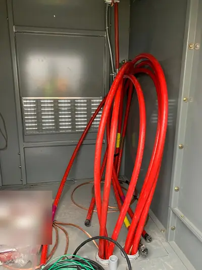 Medium-voltage cable coiled and racked inside a new cubicle ahead of termination, with the enclosure strip heater and ventilation grille behind it. A bagged parts kit on the floor is masked.