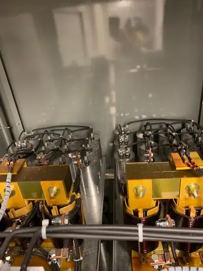 A capacitor bank inside its enclosure, cans racked above the inrush reactors with the phase connections run in insulated cable.