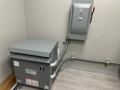 A dry-type transformer mounted beside a heavy-duty fused safety switch, primary and secondary runs made up in flexible metal conduit.