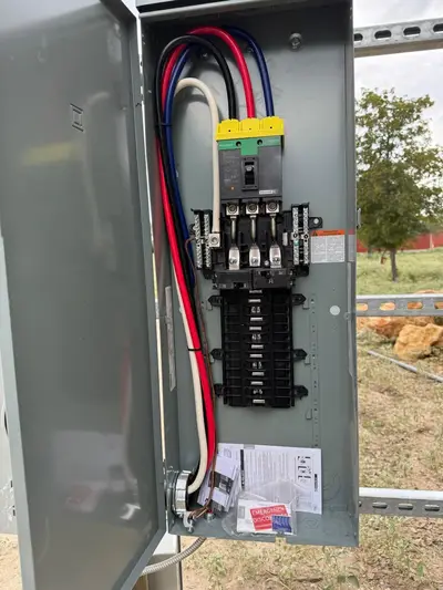 A load center mounted on the service pole with its cover off, main breaker and branch spaces visible and the instruction sheets still in the enclosure.