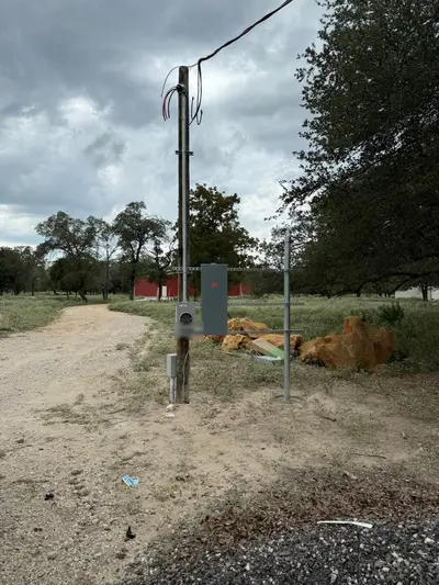 A rural overhead service: the drop landed on a mast at the head of the pole, meter enclosure and disconnect racked below on strut, branch run leaving in flexible conduit. The number stencilled on the meter can is masked.