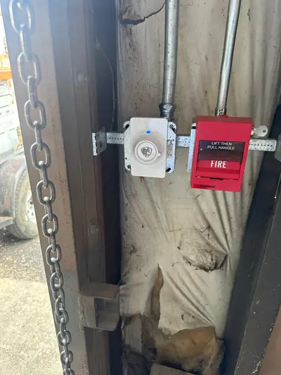A fire alarm pull station and a notification appliance mounted on a building column, conduit dropped from the deck above.