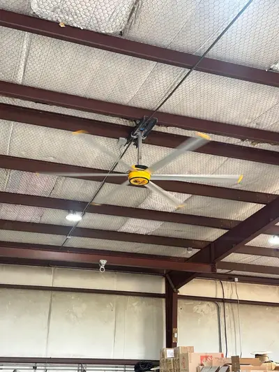 A high-volume low-speed fan turning on its mount below the ridge, with the aisle lighting run beyond it.