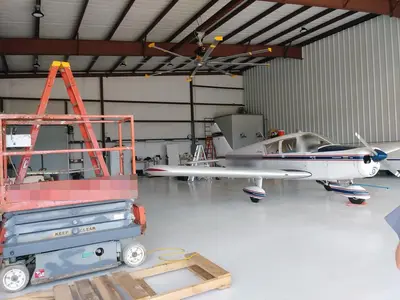 The finished hangar bay: fan, high-bay lighting and door track above a light aircraft parked inside. Aircraft registrations are masked.