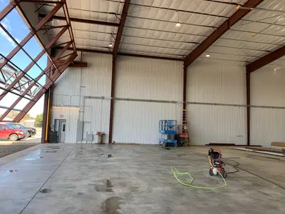 A hangar bay with the roof framing exposed and the lighting run along the purlins, doors open to the apron.