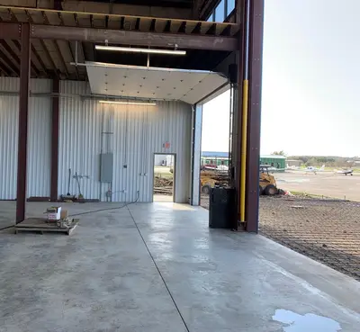 The hangar's side bay with the door open to the apron, the panel and its feed run on the back wall and an exit sign above the man door.