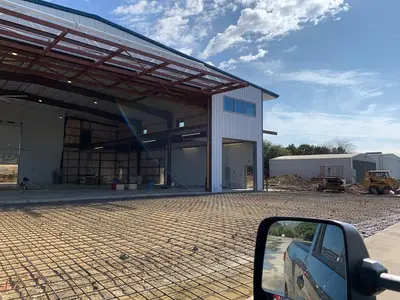 The hangar exterior with its office tower, seen across the slab reinforcement. A window graphic and a figure inside the bay are masked.