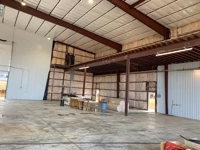 The hangar interior at insulation stage: mezzanine steel in place, a strip fixture run along the beam and the panel set on the column. A banner on the wall is masked.